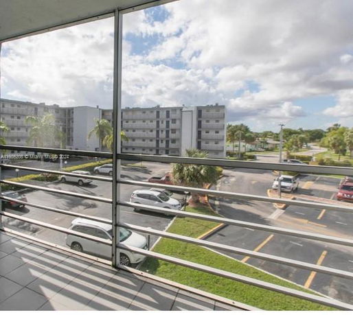 View from a balcony overlooking a parking area and apartment buildings.