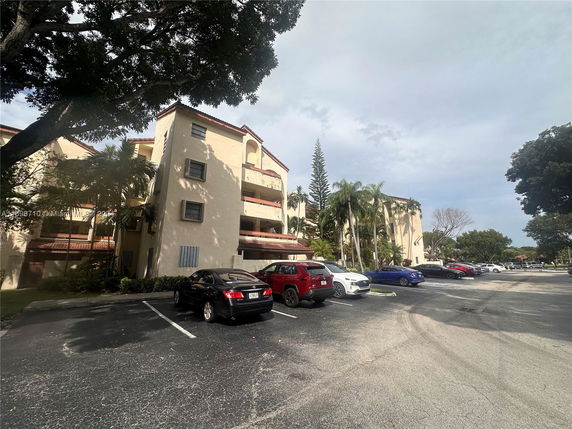 Parking area in front of a multi-story residential building with several parked cars.