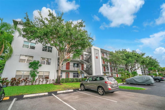 Front view of a multi-story residential building with outdoor staircases and visible parking area.