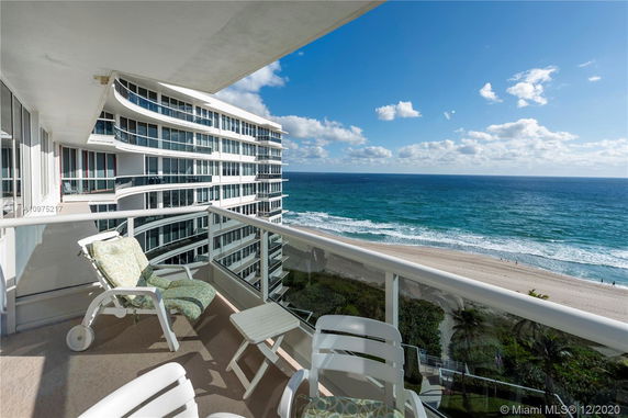 View from a balcony overlooking the ocean and beach, with a nearby modern building.