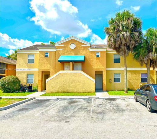 Front view of a two-story residential building with a yellow exterior and blue awnings over the entrance.