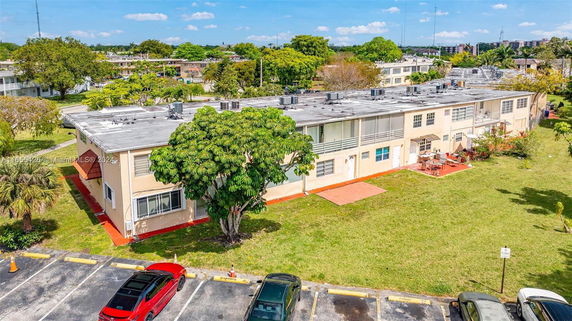 Aerial view of a two-story residential building with a flat roof, surrounded by greenery and a parking area.