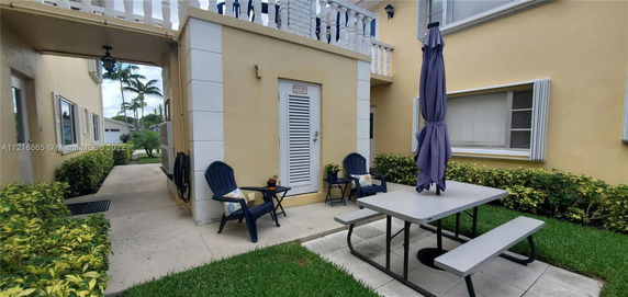 Outdoor area with a picnic table and chairs near a light-colored building with plants along the walkway.