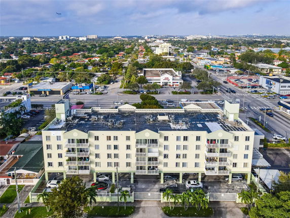 Aerial view of a multi-story residential building with balconies, located on a busy street corner surrounded by commercial and residential areas.