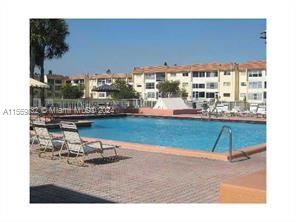 Outdoor swimming pool area with lounge chairs and apartment buildings in the background.