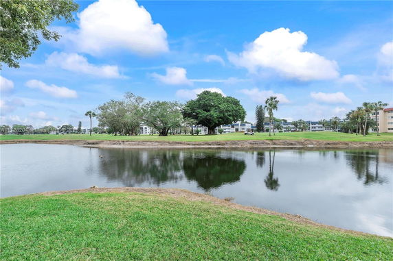 A scenic view of a pond with trees and residential buildings in the background.