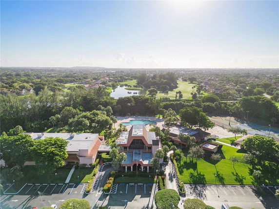 Aerial view of a complex with buildings, parking area, pool, and landscaped surroundings.