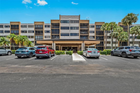 Front view of a multi-story apartment building with a covered entrance and parking area.