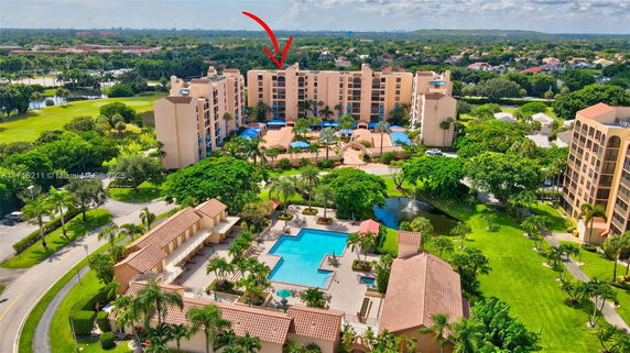 Aerial view of a multi-story residential complex with a central pool area and surrounding greenery.