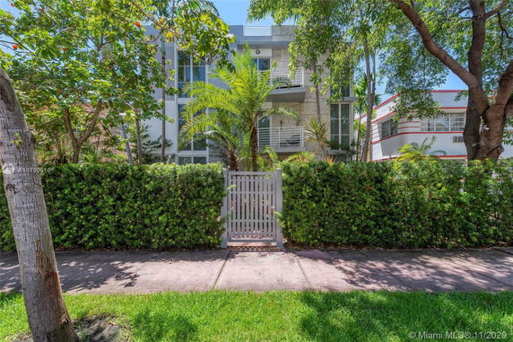 Front view of a modern multi-story building with a gate and lush greenery.