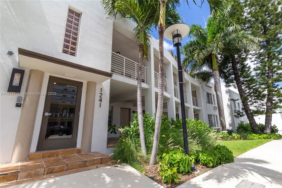 Front view of a modern multi-story building with balconies and a glass door entrance.