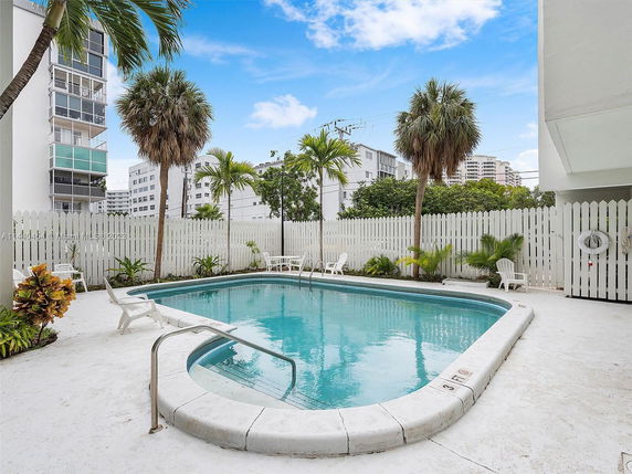 Outdoor swimming pool with surrounding white fence and palm trees.