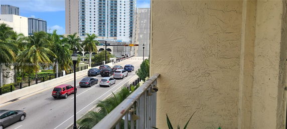 View from a building showing traffic on a road with palm trees and high-rise buildings in the background.