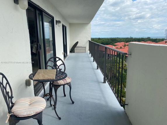 Outdoor balcony with metal chairs and table, overlooking rooftops and greenery.