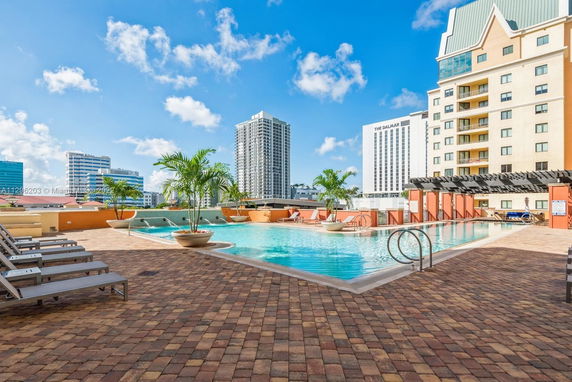 Outdoor rooftop swimming pool with lounge chairs and planters, surrounded by city buildings.