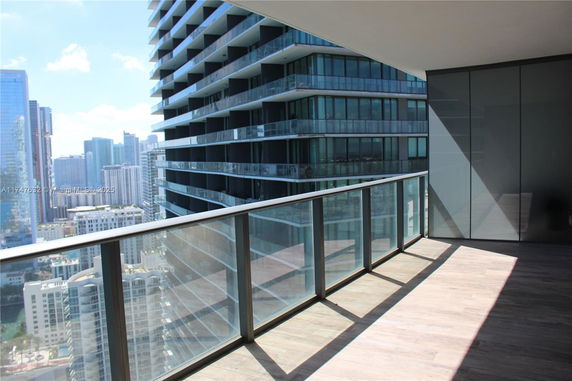 Balcony with glass railing offering a view of modern high-rise buildings.
