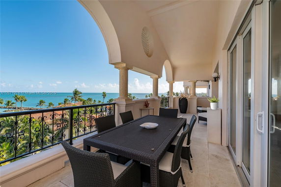 Covered balcony with dining table overlooking ocean and palm trees.
