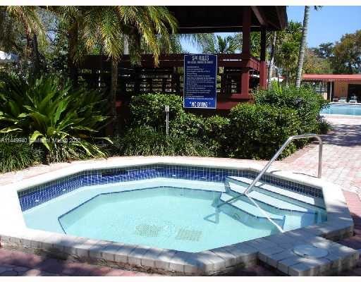 Outdoor view of a jacuzzi with nearby greenery and a pool visible in the background.