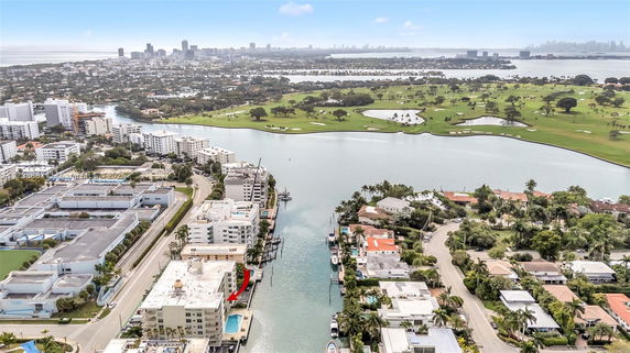 Panoramic view of a cityscape with waterways and buildings, featuring a golf course and distant city skyline.