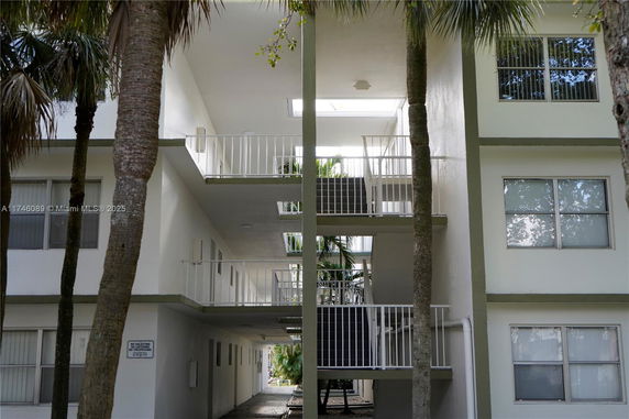 Front view of a multi-story apartment building with open walkways and trees in front.