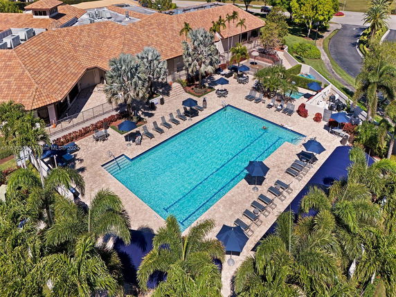 Aerial view of a building with a tiled roof and a large outdoor swimming pool area surrounded by lounge chairs and umbrellas.