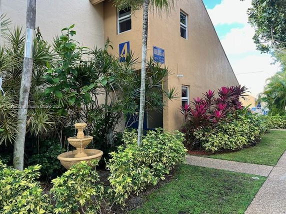 Front view of a beige building with small windows and a surrounding garden area.