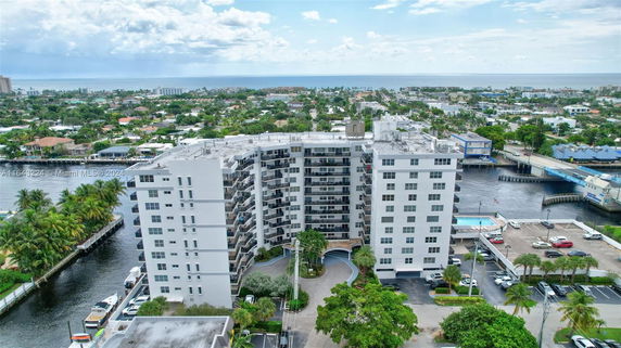 Aerial view of a large multi-story apartment building near a waterway, surrounded by a suburban area and close to the ocean.