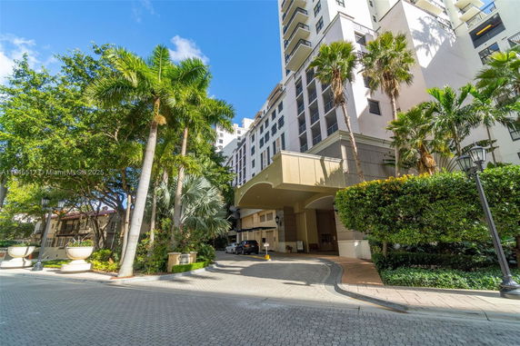 Front view of a multi-story building with a driveway and tall palm trees.