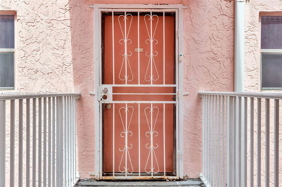 Front view of an apartment entrance with a pink textured wall and white metal security door.