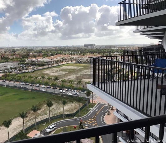 View of surrounding areas from a high balcony, with roads, greenery, and distant buildings visible.