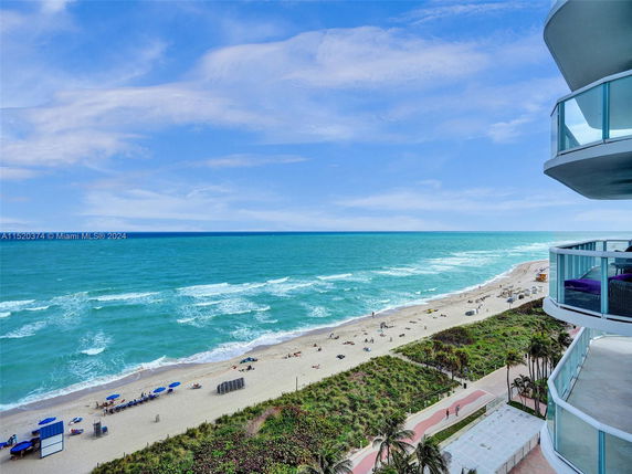 Balcony view overlooking a sandy beach with turquoise ocean waves and scattered beachgoers.