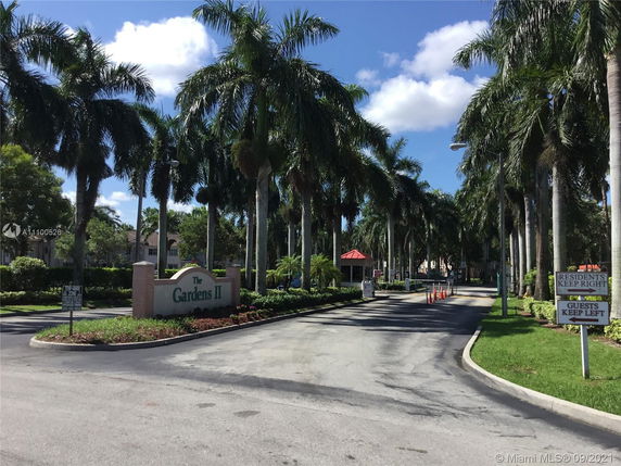 Entrance to a residential area with palm trees and a sign for The Gardens II.