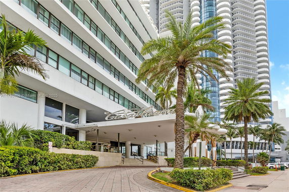 Front view of a multi-story building with a modern facade and palm trees in the foreground.