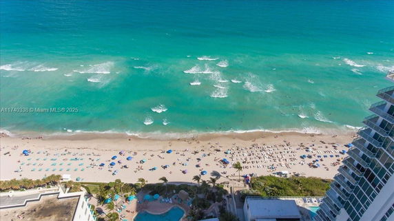 Aerial view of a beachfront area with ocean waves and a sandy beach filled with umbrellas and lounge chairs.