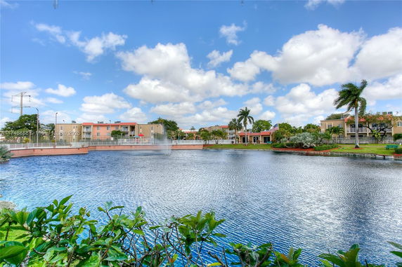 View of buildings across a lake with palm trees and a blue sky.