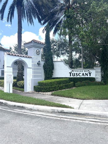 Front view of a building entrance with signage reading 'Villas de Tuscany' and surrounded by palm trees and hedges.