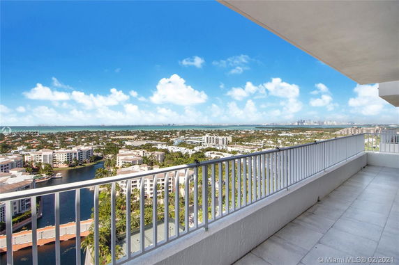 Panoramic view from a high-rise balcony overlooking a cityscape and body of water.