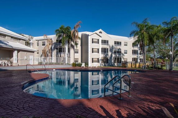 Outdoor swimming pool area in front of a multi-story residential building.