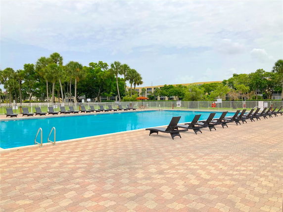 Outdoor swimming pool area with lounge chairs on a paved deck.