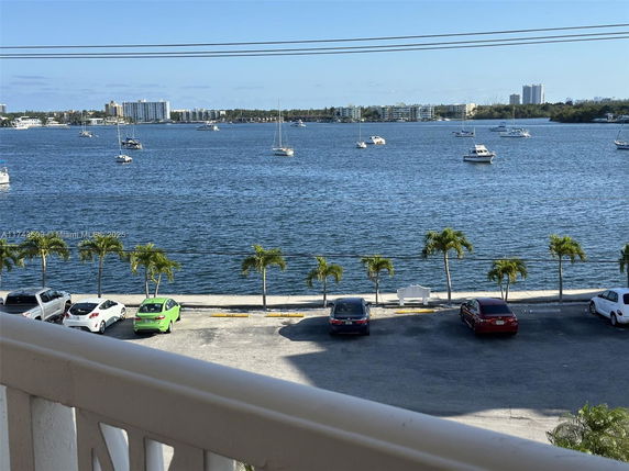 Panoramic view of a waterfront area with boats on the water and parked cars along the shore.