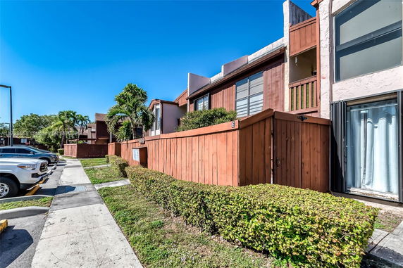 Front view of a multi-story residential building with wooden fencing and a row of parked cars.