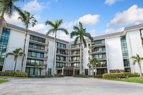 Front view of a multi-story apartment building with balconies and palm trees.