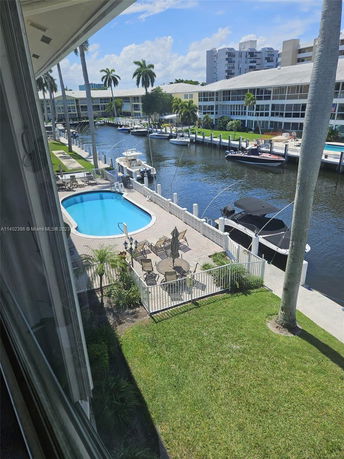 View of a canal with several small boats docked beside multi-story buildings. There is a small pool and a seating area with umbrellas visible in the foreground.