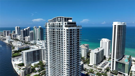 Aerial view of high-rise buildings near the coastline, with a prominent white multi-story building in the foreground.