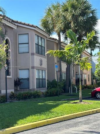 Front view of a two-story residential building with beige exterior and palm trees in front.