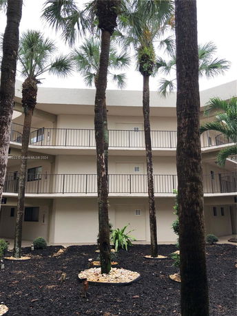 Exterior view of a three-story building with balconies and palm trees in the foreground.