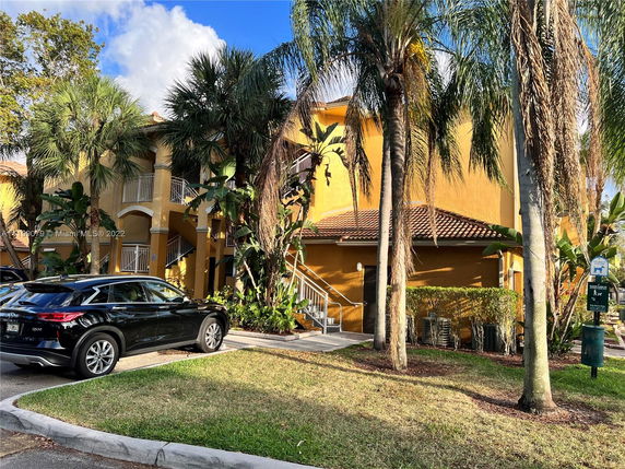 Front view of a two-story building with outdoor stairs and palm trees.