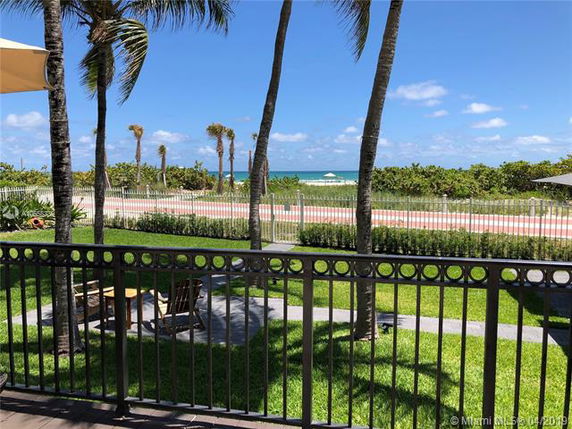 View of the beach and ocean from a fenced outdoor area with palm trees.