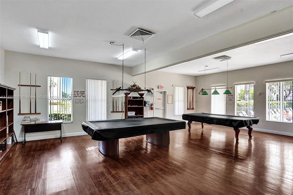 Room with pool tables and accessories, wooden floor and ample natural lighting.