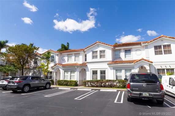 Front view of a two-story townhouse with white walls and red-tiled roof, featuring parking spaces in front.
